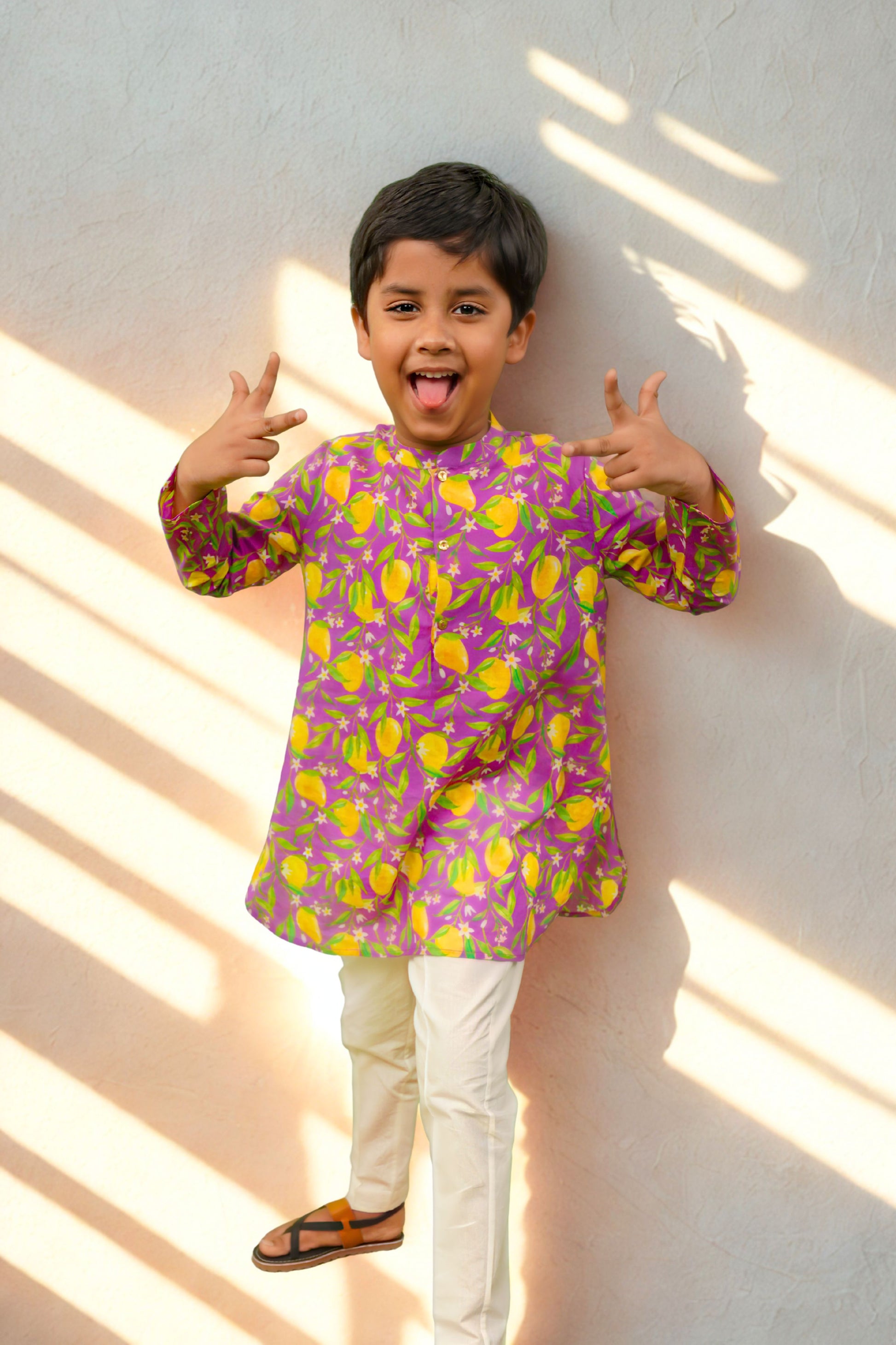 Child wearing a colorful kurta with lemon pattern against a white wall.